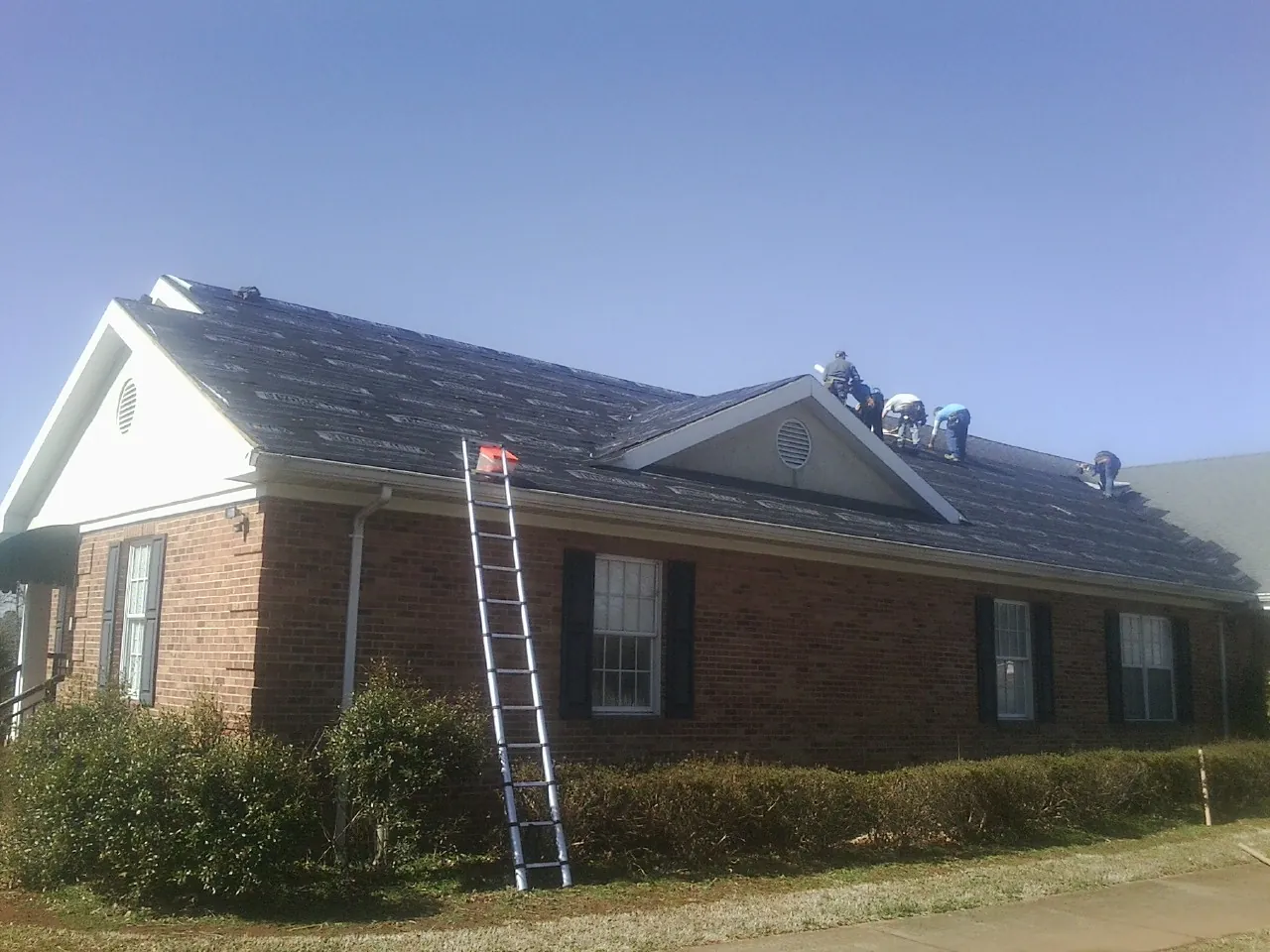 Crew tearing shingles off a brick ranch roof with a ladder set — Metal Roof Repair work by our crew in Wilberforce