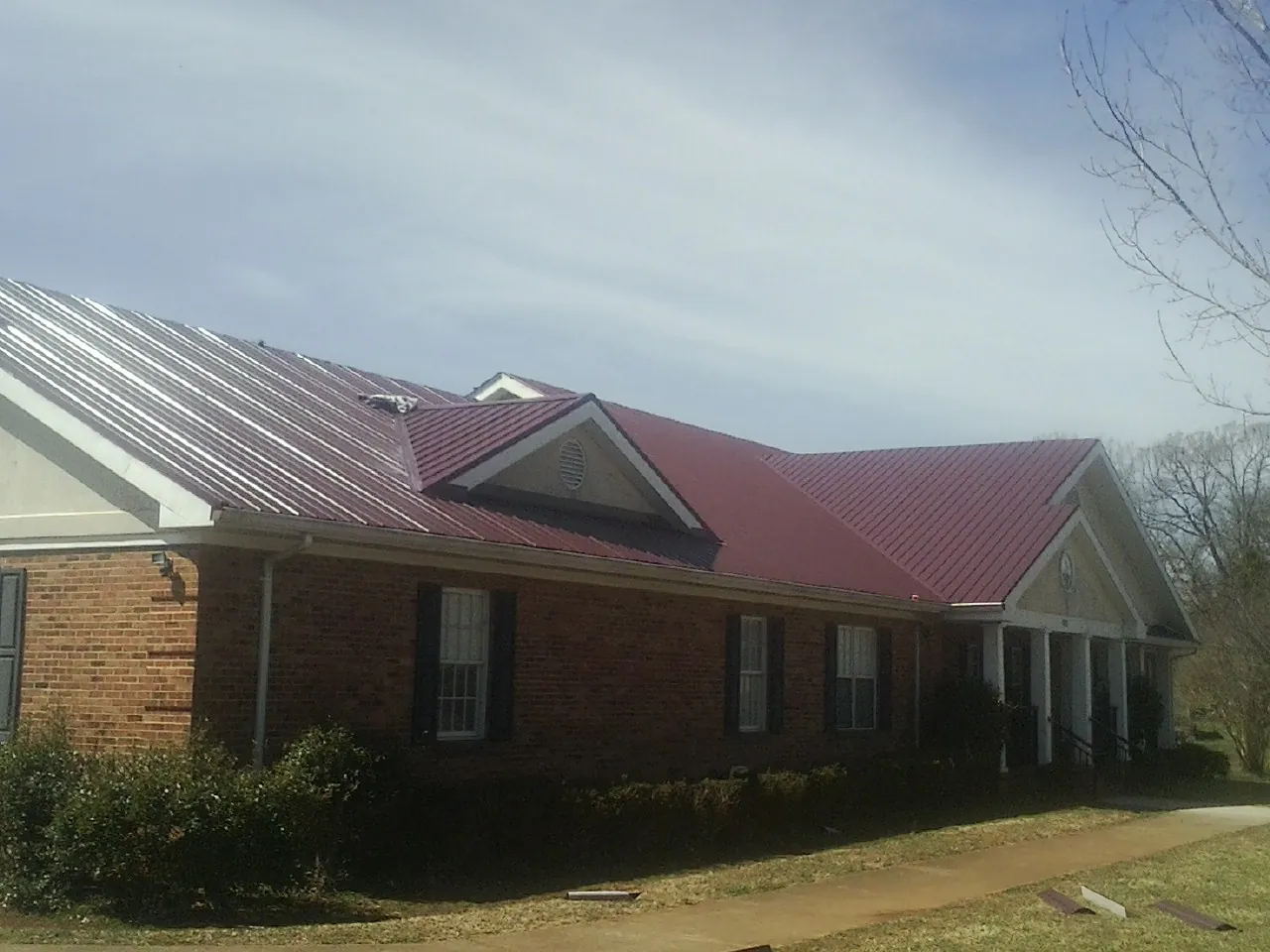 Red metal roof with gabled entries on a long brick building, from a Hail Damage Roof Repair job in Wilberforce