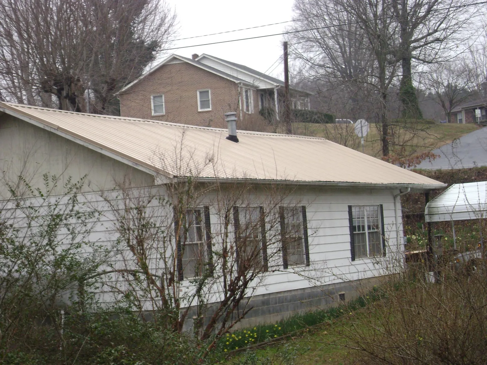 Tan metal roof on a white sided house set into a hillside — Commercial Roofing by Roofing Brothers in Wilberforce